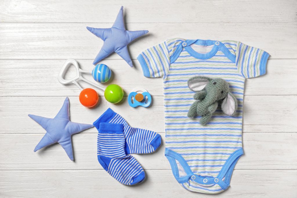 Blue baby romper with an elephant stuffed animal, blue socks, stars and toy arranged on the floor