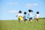 Four children running on a grass field on a sunny day