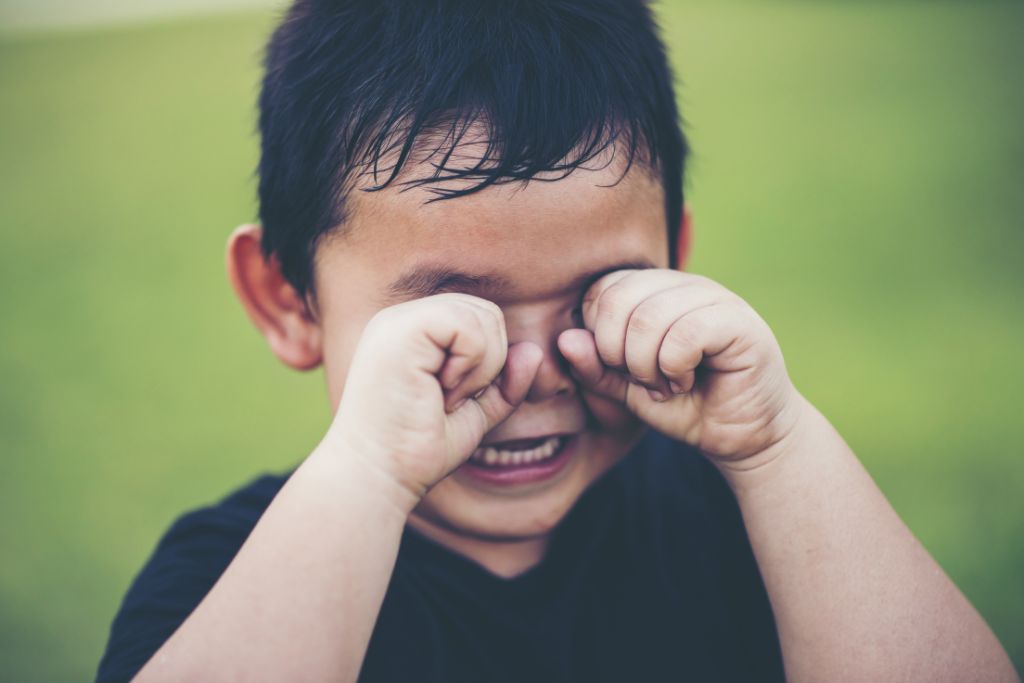 A dark haired boy crying and rubbing his eyes.