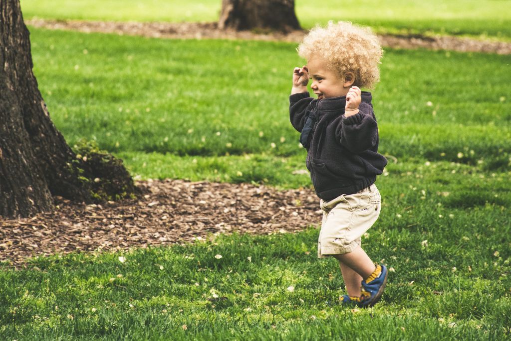 Toddler running on a grass with his hands up